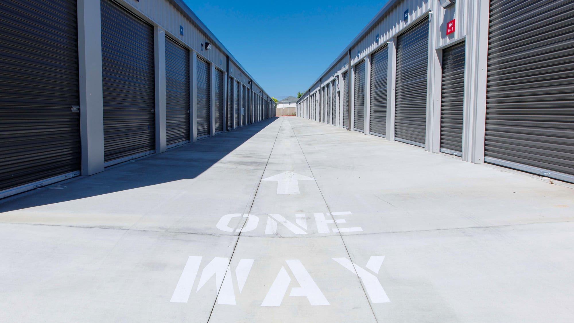 A wide, one-way concrete driveway between two facing rows of drive-up storage units at Manteca Storage