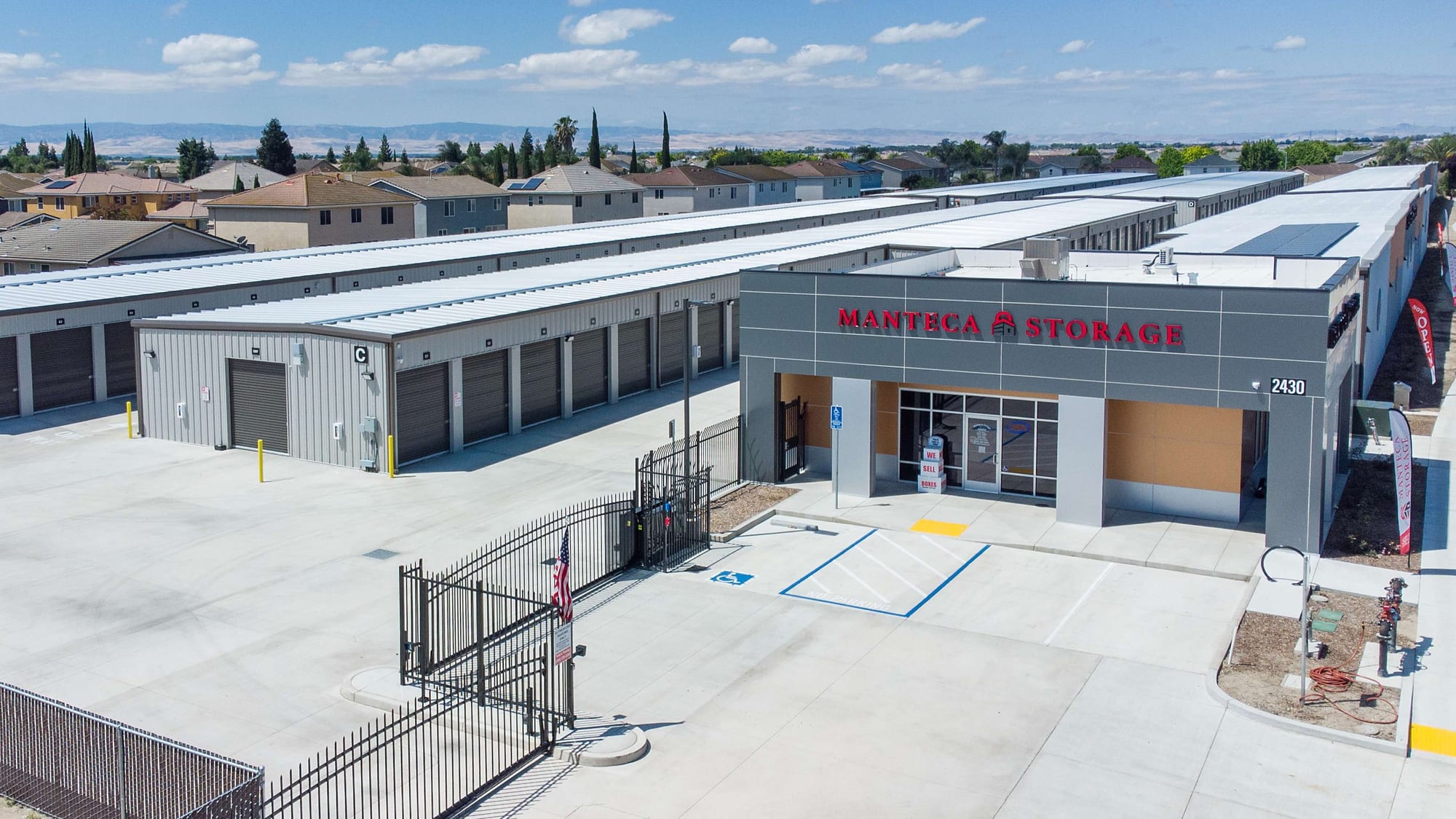 The open security gate at Manteca Storage, with the office and two drive-up unit buildings beyond