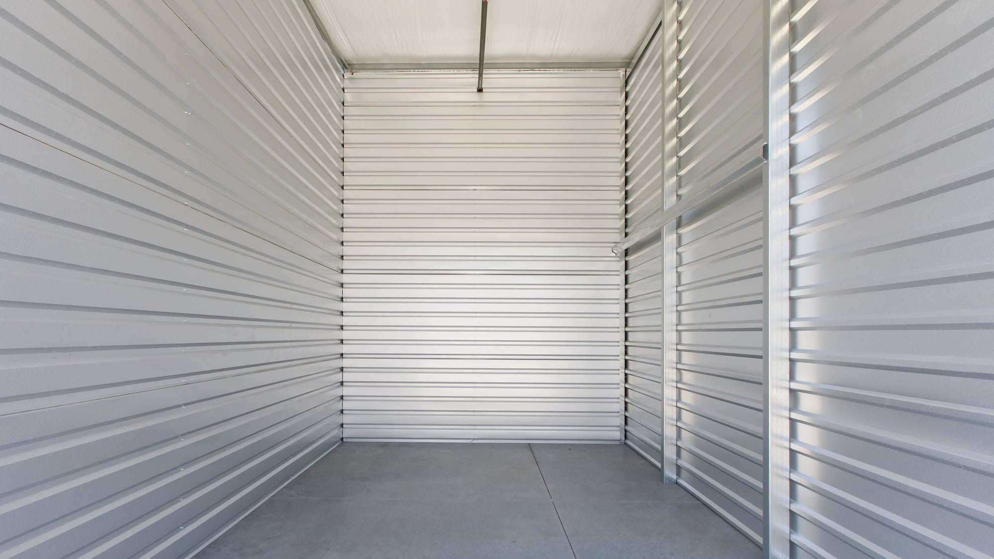 Inside an empty storage unit at Manteca Storage: bare concrete floor, sealed metal walls, and a roll-up door