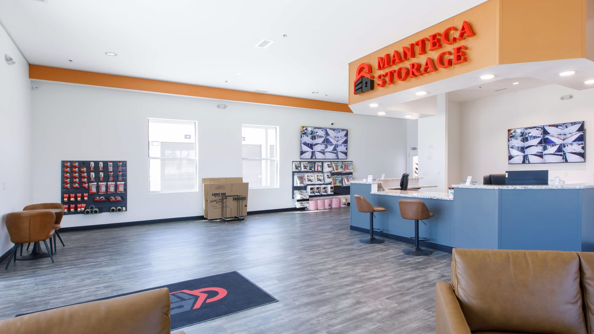 Manteca Storage's lobby: a rental counter, packing supplies for sale, and two wall monitors showing live security cameras